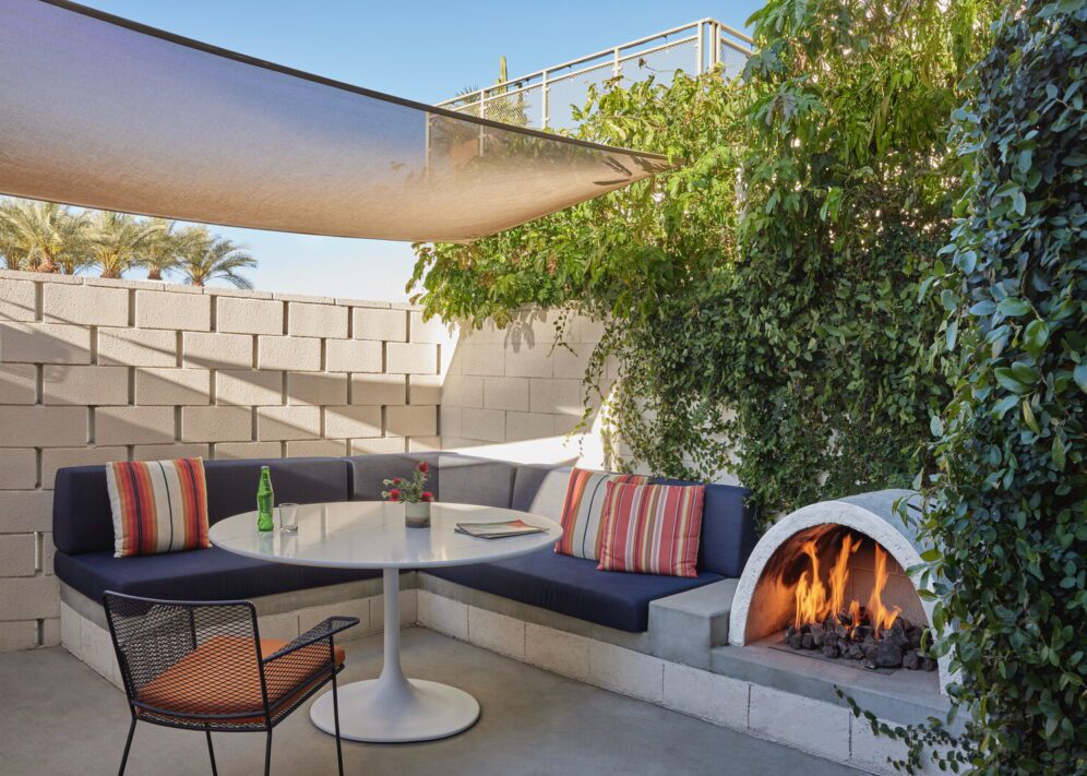 A private patio provides a sofa, table, and chair for outdoor relaxation; a small, semicircular fireplace provides warmth and ambiance