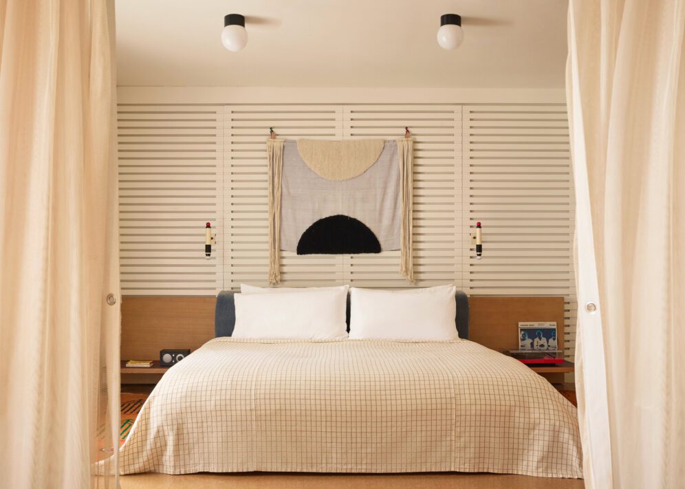 A private bedroom features a white, plaid bed flanked by a record player on one side and a radio and phone on the other